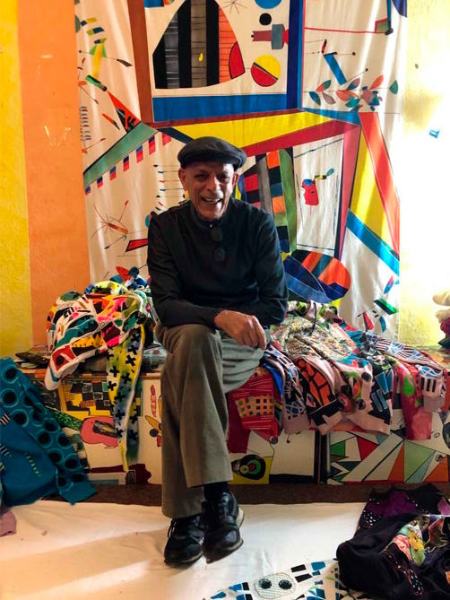 Fotografie von Hamid Zenati sitzend auf und vor bunten Stoffen