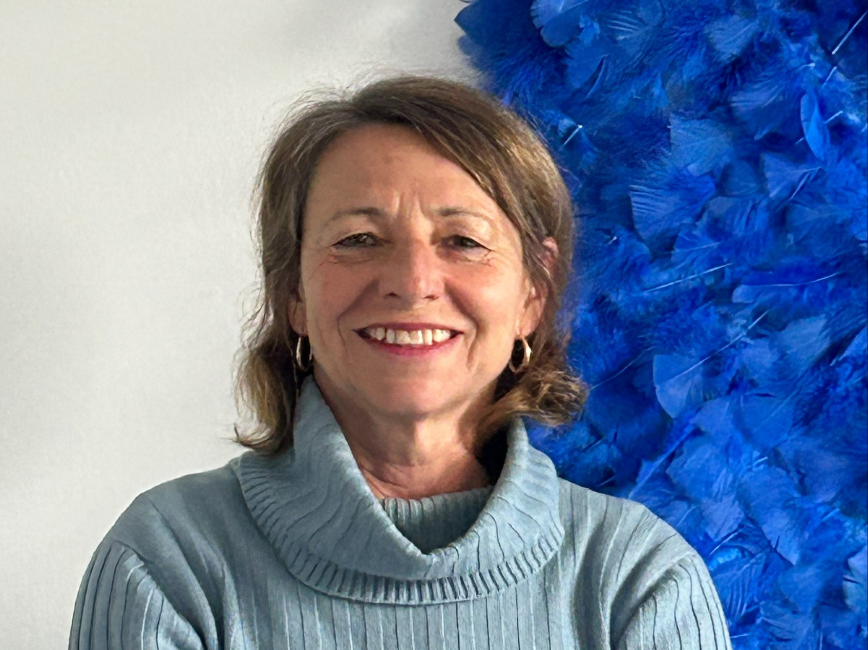 Foto von Karolina Sarbie hellblauer Pullover vor blauen Kunstwerk aus Federn